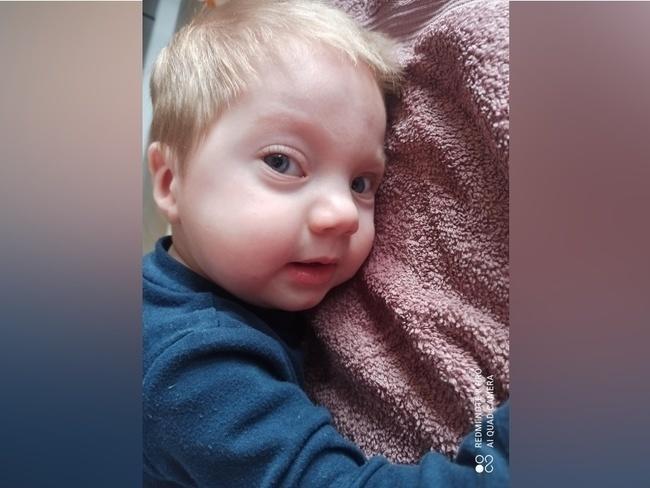 Na zdjęciu znajduje się 12 miesięczny chłopiec który leży na brzuchu z twarzą zwróconą w obiektyw. Chłopiec ma blond włosy oraz granatowy sweterek.