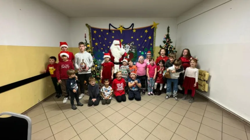 Zdjęcie grupowe dzieci z Mikołajem. Część dzieci ma ubrane czapki Mikołaja w rękach trzymają paczki