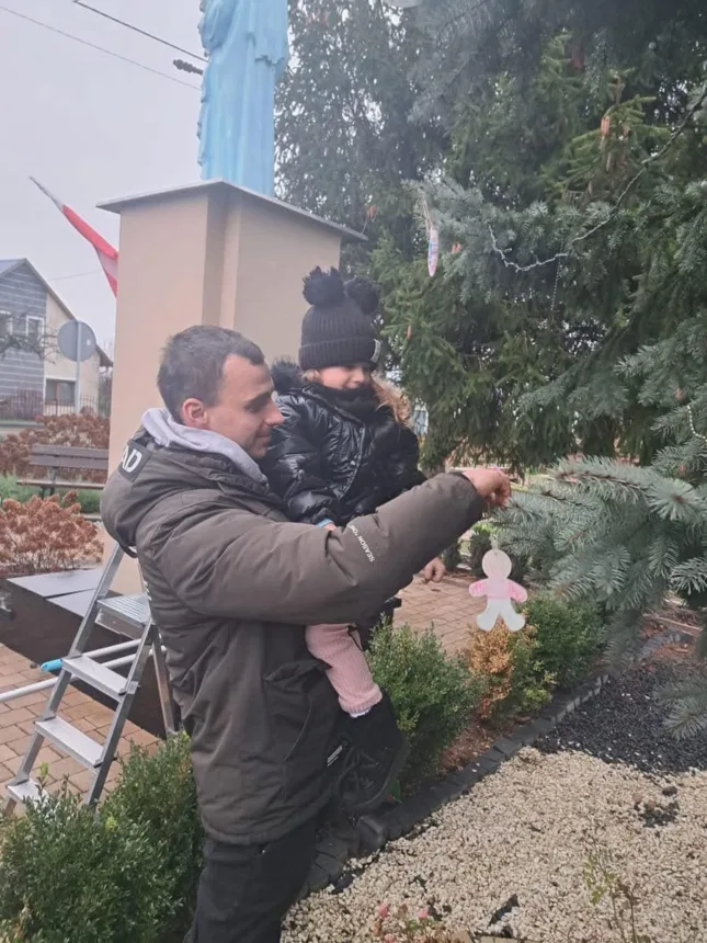 Zdjęcie dziewczynki z tatą podczas zawieszania bombki na choinkę