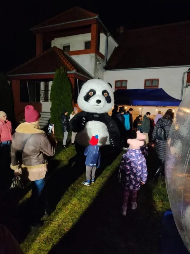 Na pierwszym planie duża panda a wokół niej biegają dzieci